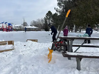 outdoor rink in a park with kids skating, shovel in foreground