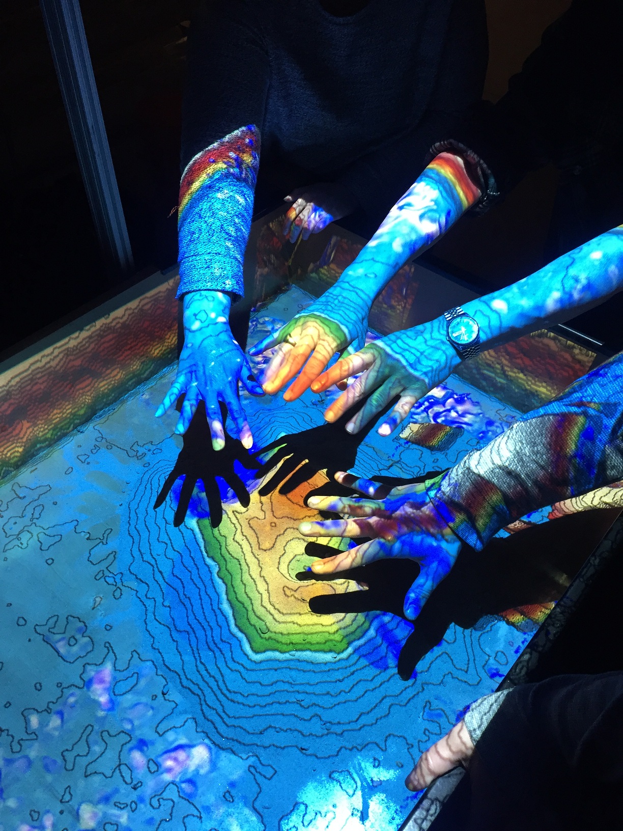 Arms and hands extending over a table with a blue and yellow light projecting onto the arms and hands